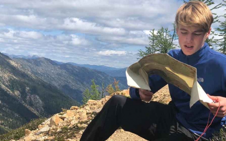 a teen reads a map while sitting on a rock overlooking a mountainous landscape in the pacific northwest